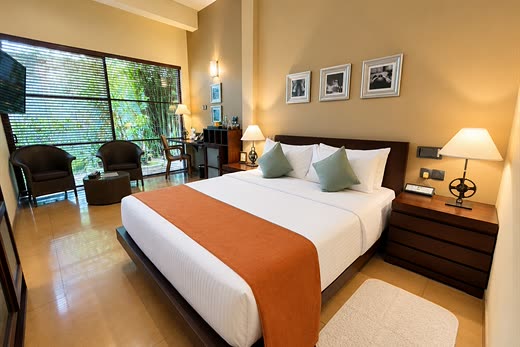 A Deluxe Room at Colombo Court with a queen bed and armchairs at a tall window onto the garden.