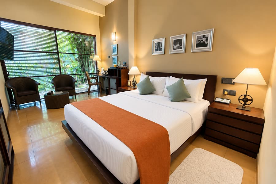 A Deluxe Room at Colombo Court with a queen bed and armchairs at a tall window onto the garden.