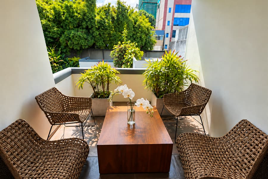 Two cane chairs and a table on the balcony outside a Deluxe Room, orchids on the table and greenery beyond.