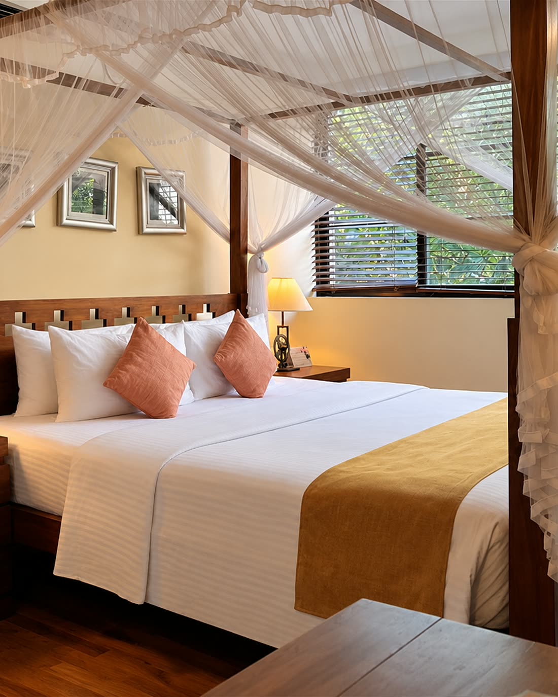 The four-poster bed in the Luxury Duplex Suite, white net tied back and the window of greenery beyond.