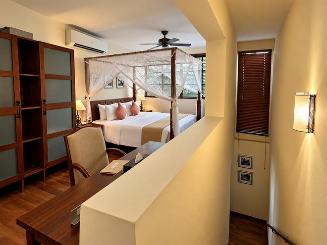 The bedroom of the Luxury Duplex Suite seen from the stair, the four-poster bed beside timber blinds.