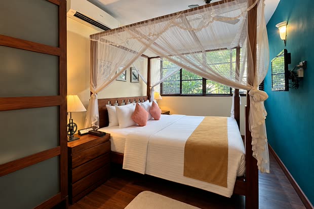 The Luxury Duplex Suite at Colombo Court, a four-poster bed under a white net beside a teal wall and a window of trees.