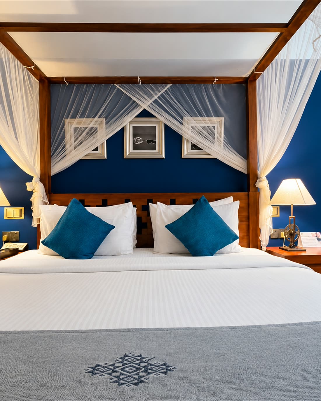 The four-poster bed in the Luxury Honeymoon Suite, framed photographs on the blue wall above it.