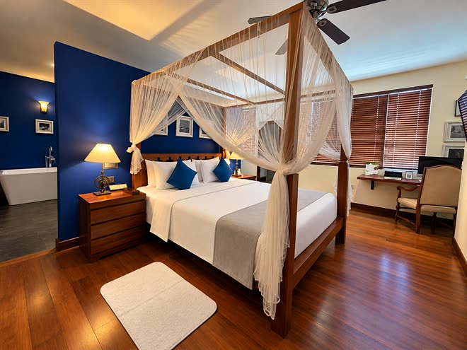 The Luxury Honeymoon Suite seen wide, the four-poster bed, the standing bath and the desk at the window.