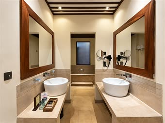 The bathroom in a Luxury Junior Suite, twin basins on stone counters under timber mirrors, the shower beyond.