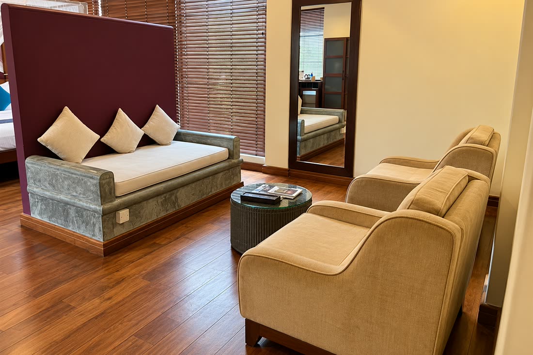 The sitting area in a Luxury Junior Suite, a daybed and two armchairs on timber floors beside the blinds.