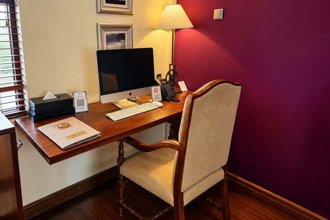 The writing desk in a Luxury Junior Suite, a timber desk, a screen and a leather-seated chair against the plum wall.