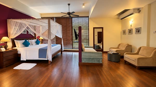 A Luxury Junior Suite at Colombo Court seen wide, the four-poster bed under its net, a daybed and armchairs, and windows into the trees.