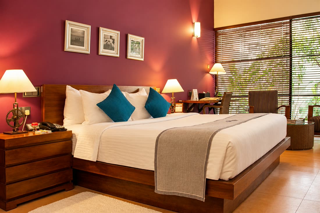 A Superior Deluxe room with a king bed, teal cushions and framed prints on the plum wall.