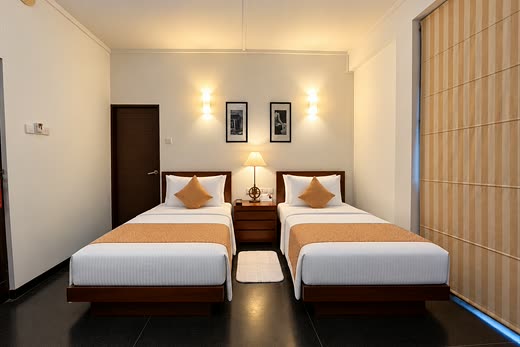 A Deluxe Twin room at Colombo Court, two single beds with orange runners under a pair of wall lamps.