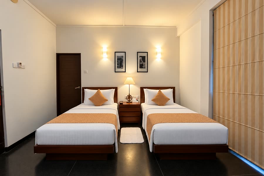 A Deluxe Twin room at Colombo Court, two single beds with orange runners under a pair of wall lamps.