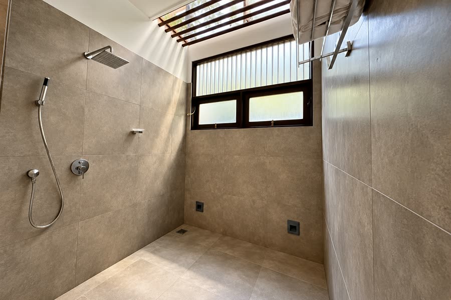 The walk-in shower in a Deluxe Twin room, stone tiles lit from a skylight above.
