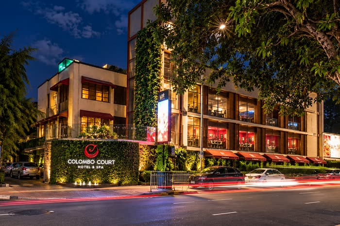 Colombo Court Hotel & Spa at night, the glass tower wrapped in climbing plants and the sign lit above the lane.