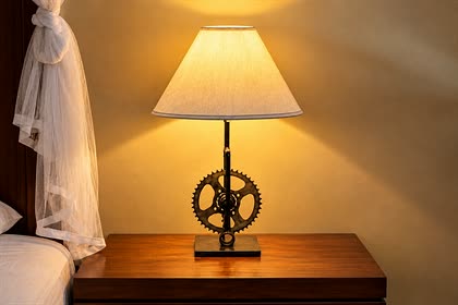 A bedside lamp at Colombo Court with a stand made from an old bicycle sprocket, the shade lit warm.