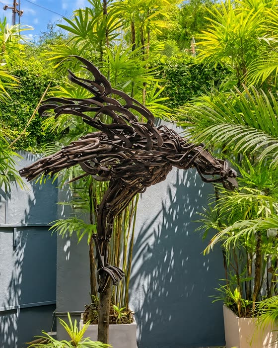A bird sculpted from pieces of scrap metal among palms in the garden at Colombo Court.