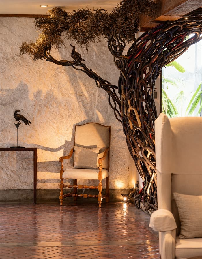 The lobby at Colombo Court, a winged armchair beneath the tree sculpted from scrap steel, warm light on the brick floor.
