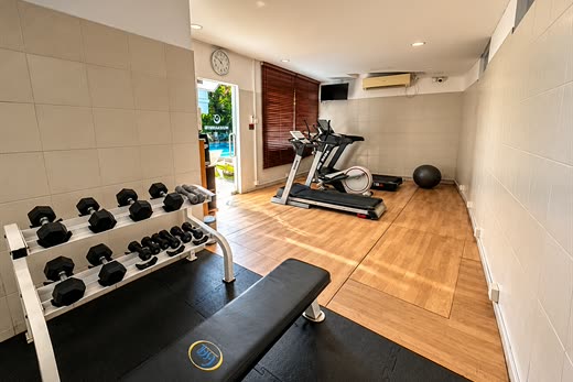 The gym at Colombo Court, a rack of dumbbells and a bench with the treadmill and the pool through the window.