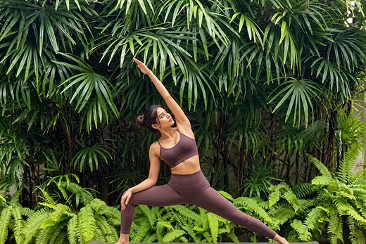 A guest holding a standing yoga pose against a wall of palms and ferns in the garden at Colombo Court.