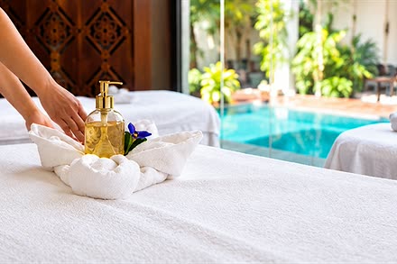 A therapist setting a folded towel and a bottle of oil on a treatment bed at The Court Spa, the plunge pool behind.