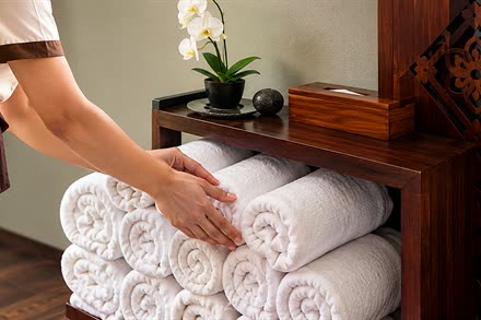 A therapist placing rolled white towels beneath the timber cabinet at The Court Spa, an orchid above.