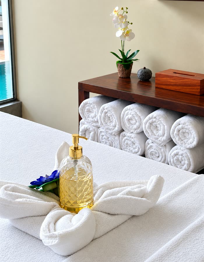 Rolled white towels and a bottle of massage oil laid out on a treatment bed at The Court Spa.