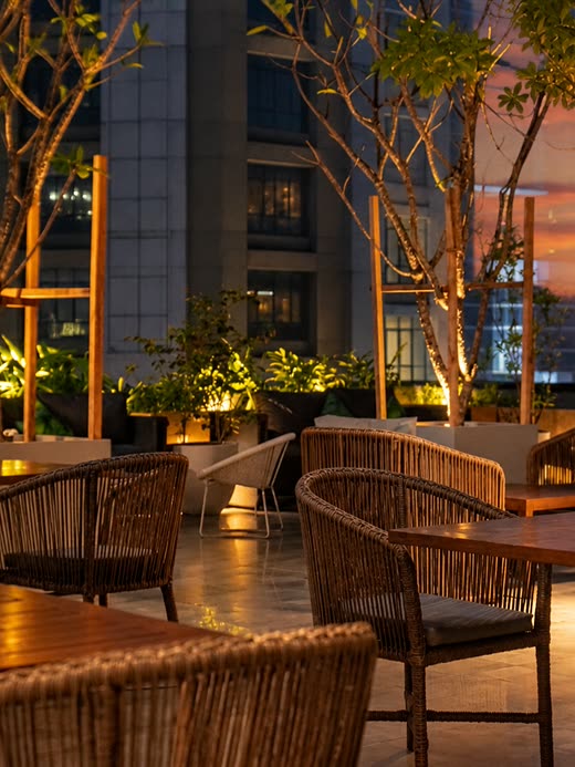 Tables on the rooftop at Cloud Caf&eacute; & Bar at twilight, trees lit from below among the planters.